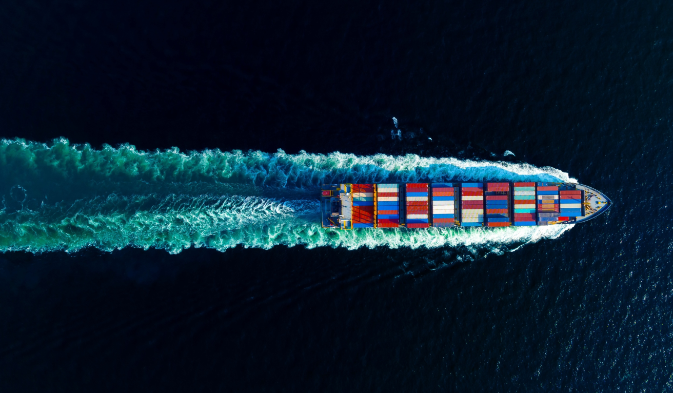 A sleek military drone is captured in flight above a rugged mountain range under a dramatic sky